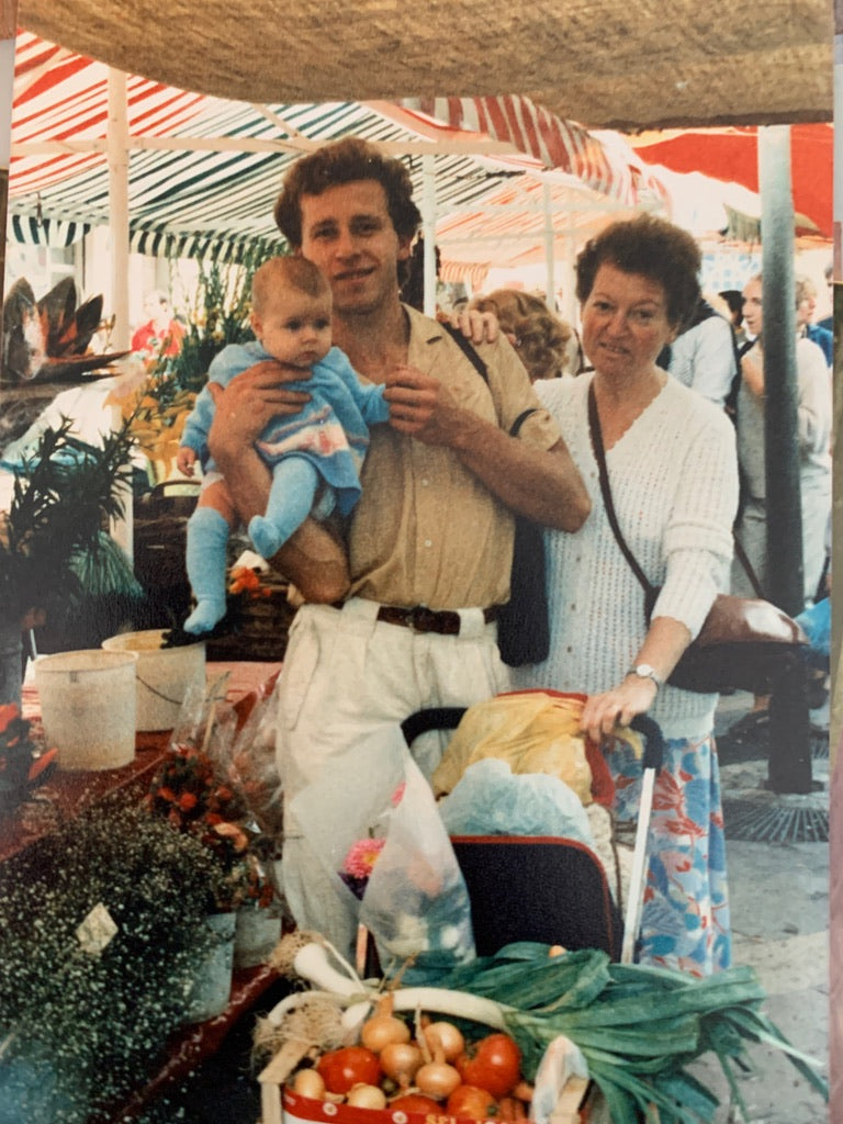 Family at the market: Laurence's mother, brother, and infant daughter at the Cours Saleya farmers market in Nice, the baby stroller filled with fresh leeks, tomatoes, and produce — three generations shopping together