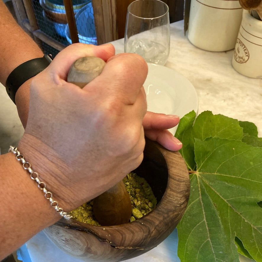  Mortar and pestle: Hands grinding fresh herbs in an olive wood mortar and pestle during a hands-on French cooking class — making persillade from scratch in Santa Barbara